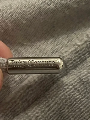 Grå Juicy Couture hoodie med dragkedja - Säljer en grå hoodie från Juicy Couture i storlek L. Tröjan har huva, snörning med metalländar och dragkedja framtill. Mjuk och skön, perfekt för chill dagar. Klassisk design med fickor på sidorna och ribbade muddar vid ärmslut och nederkant.