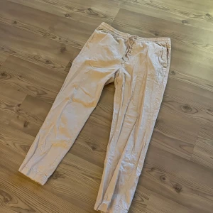 Beige linnebyxor med snörning - Snygga beige linnebyxor med elastisk midja och snörning framtill. Byxorna har en avslappnad passform och är perfekta för varmare dagar. De har fickor på sidorna och är tillverkade i ett lätt och luftigt linnematerial. Dem är väldigt små för sin storlek skulle gissa runt L-M 