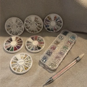 Mixade ansikts- och nagelstenar i olika färger - Säljer flera askar med ansikts- och nagelstenar i olika former och färger, inklusive silver, guld, rosa, blått och grönt. Perfekt för att skapa kreativa sminklooks eller dekorera naglar. Medföljer en applikatorpenna för enkel applicering. 