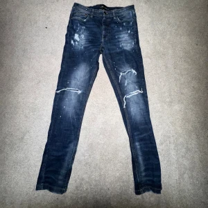 Supply & Demand jeans - Snygga mörkblå skinny jeans från Supply & Demand med slitna detaljer och färgstänk på framsidan. Jeansen har klassisk femficksdesign, dragkedja och knappstängning. Passformen är tight och materialet är jeans med stretch för extra komfort.