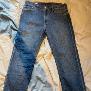 Levi's Premium 501 blå jeans - Säljer ett par klassiska Levi's Premium 501 jeans i mörkblå denim. Modellen har raka ben, fem fickor och knappgylf. Snygga kontrastsömmar och ikonisk läderpatch baktill. Perfekt för dig som gillar tidlös stil och äkta denim.