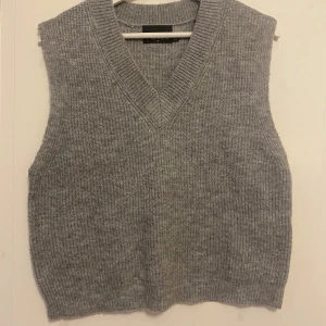 Grå stickad väst med v-ringning - Snygg grå stickad väst från Pieces med bred ribbad v-ringning. Perfekt att slänga över en skjorta eller t-shirt för en chill och trendig look. Mjuk och skön kvalitet som håller dig varm under kyliga dagar.