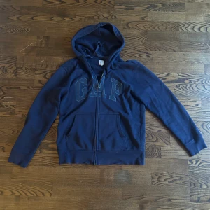 Marinblå zip up hoodie från GAP - Säljer en marinblå zip up hoodie från GAP i storlek S. Tröjan har dragkedja framtill, huva med snörning och två fickor. GAP-loggan är broderad på bröstet. Materialet är mjuk bomull, perfekt för chill dagar. Långärmad och klassisk passform.