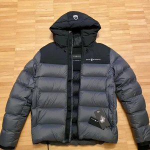 Grå dunjacka med huva från Sail Racing - Säljer en helt ny Sailracing jacka då den inte passade mig och blev av med kvittot. Har försökt bli av med den länge därav det billiga priset så passa på! (Nypris  ca. 3500kr)