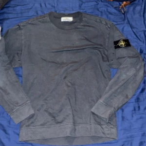 Svart långärmad tröja Stone Island - Säljer en svart långärmad tröja från Stone Island med klassisk rund hals och ikonisk logotyp-patch på vänster ärm. Tröjan är i mjuk bomull och har en clean, stilren look som passar perfekt till streetwear eller casual outfits. Priset är ej hugget i sten.