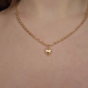 Guldigt halsband med hjärthänge - Snyggt halsband i guldton med dubbla kedjor och ett gulligt hjärthänge. Hänget har en liten hjärtformad detalj i mitten och en pärlad kant runt om. Perfekt för dig som gillar romantiska smycken med lite extra bling.