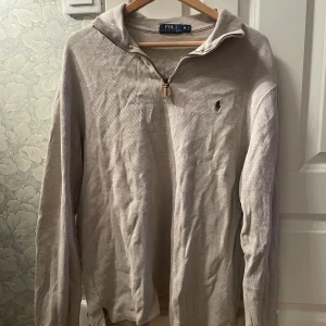 Beige half zip tröja Polo Ralph Lauren - Säljer en beige långärmad tröja från Polo Ralph Lauren med half zip och klassisk krage. Tröjan har det ikoniska broderade logotypen på bröstet och är tillverkad i mjuk bomull. Perfekt för lager-på-lager och chill stil.