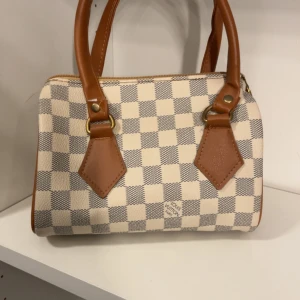 Handväska - Snygg handväska i klassiskt rutigt mönster. Väskan är beige och grå med bruna skinnhandtag och detaljer i guld. Köpt secondhand, skriv för fler bilder!💗