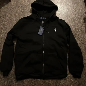 Svart hoodie från Polo Ralph Lauren - Tyget på denna hoodie är lite annorlunda än vanligt – det har en mjuk, bomullslik känsla och känns riktigt exklusivt. Observera att retur tyvärr inte är möjlig på denna vara, så var säker innan du bestämmer dig för att köpa.