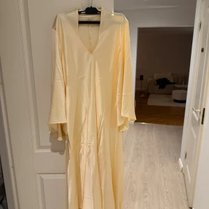 Gul långklänning Mango - Långklänning från Mango i en lyxig gul färg med glansig finish. Klänningen har v-ringning, vida ärmar och ett flowy fall. Tillverkad i ett satinliknande material som känns mjukt mot huden. Köpt för 1000, aldrig använt. Har en liten svart prick (se bild)