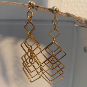 Geometriska guldiga örhängen - Unika örhängen i guldton med flera sammanlänkade fyrkantiga former som ger en cool geometrisk look. Hängande design med små och stora kvadrater i metall, Ca 6.5 cm långa
