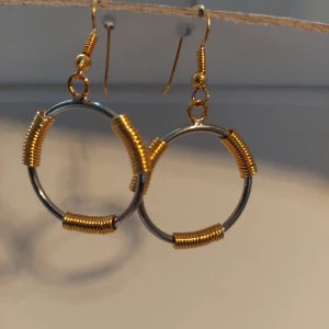 Runda örhängen med gulddetaljer - Unika örhängen i rund form med silverfärgade ringar dekorerade med guldfärgade spiraler. Designen är modern och cool, perfekt för dig som gillar att sticka ut med accessoarer. Örhängena har krokar i guldfärg och en industriell vibe. Ca 2.5 cm i diametern