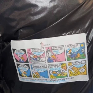 Svart Moncler pufferjacka med huva - Svart pufferjacka från Moncler med glansig finish och huva. Jackan har ett broderat Moncler-märke på ärmen, praktisk ficka med knapp och klassisk quiltad design. Materialet är syntet och dun, perfekt för kalla dagar. Snygg och tidlös look som funkar till allt.