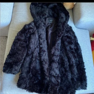 Svart pälsjacka med huva från Zara - Säljer en svart fluffig pälsjacka från Zara Trafaluc med huva. Jackan är långärmad och har en loose passform, perfekt för dig som vill ha en mysig och cool look. Materialet är syntetpäls och insidan är fodrad för extra komfort.mycket bra skick knappt använd.