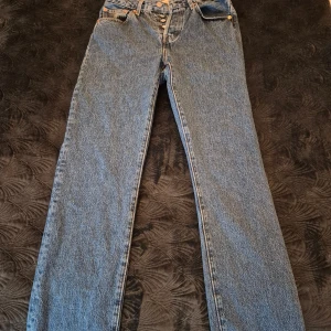 Levi's 501 jeans W27 L30 blå - Klassiska Levi's 501 jeans i blå denim med raka ben och knappgylf. Modellen har fem fickor och den ikoniska läderpatchen bak i midjan. Perfekta för dig som gillar tidlös stil och vill ha ett par jeans som funkar till allt. Endast använda 1 gång då dom var för store för mig!