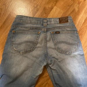 Bootcut jeans från Lee ljusblå - Snygga ljusblå bootcut jeans från Lee med klassisk femficksdesign och tydliga slitningar för en cool vintagekänsla. Jeansen har låg midja, dragkedja och bälteshällor. Perfekt för dig som gillar retrostil och bekväma jeans. De är uppsprättade längst ner!!