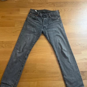 Levi's 501 grå jeans straight fit - Tja Säljer ett par klassiska Levi's 501 jeans i grå  med raka ben och fem fickor.  Jeansen har knappgylf och den ikoniska läderpatchen bak i midjan. Perfekt för dig som gillar tidlös stil och vill ha ett par jeans som funkar till allt. Har använt de ett par gånger, men har inte någon användning av de längre. 