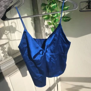 Blå satin linnetopp med rosett - Snygg blå linnetopp i satin med smala axelband. På sista bilden så ser man att höger sida så viker den ner sig typ (den va så när jag köpte den) jag har använt toppen en gång o då vek jag ner den bara o på mig så funkade det. Men man tänker inte på de om man är ute på kvällen eller så. Den är S men passar XS oxå
