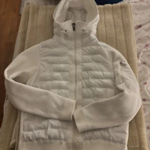 Vit pufferjacka från Moncler L - Säljer en snygg vit pufferjacka från Moncler i storlek L men skulle säga att den passar folk i M för tycker inte den är så stor! Jackan har huva med snörning, quiltad front och ribbade ärmar. Dragkedja framtill och Moncler-logga på ärmen. Perfekt för dig som gillar stilren och exklusiv look. Skriv till mig om ni vill se bild på två skador som inte syns väl,  men skriv om ni vill se de!