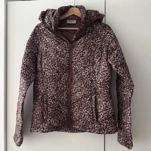 Leopardmönstrad pufferjacka Wados  - Säljer en brun leopardmönstrad pufferjacka från Wados i storlek M. Jackan har huva, dragkedja framtill och två fickor med dragkedja. Perfekt för dig som vill sticka ut med ett djuriskt mönster och hålla dig varm under höst och vinter.