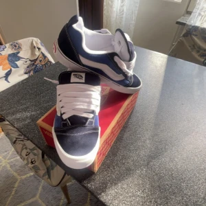 Vans knu skool  - Säljer ett par klassiska Vans Old Skool sneakers i marinblått och vitt. Skorna har vit sula, vit sidestripe och vita snören. Ovandelen är i mocka och canvas med tydliga kontrastsömmar. Perfekta för dig som gillar streetstyle och skatekänsla. Storlek 42 men passar upptill ca 44.5