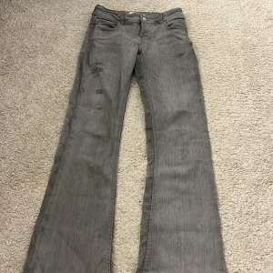 Grå bootcut jeans från Gina Tricot - Snygga grå jeans från Gina Tricot i storlek 158. Modellen har bootcut-ben och klassisk femficksdesign. Jeansen har dekorativa sömmar och slitningar på låret .Tillverkade i mjukt bomullsmaterial med knappstängning framtill.