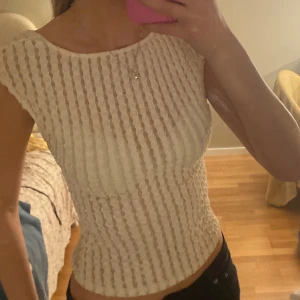 Vit ribbad topp med öppen rygg - Säljer en vit ribbad topp med korta ärmar och snygg öppen rygg. Toppen har ett vertikalt randigt mönster och är figurnära med croppad passform. Perfekt för dig som gillar stilrena detaljer och vill ha något som sticker ut lite extra.