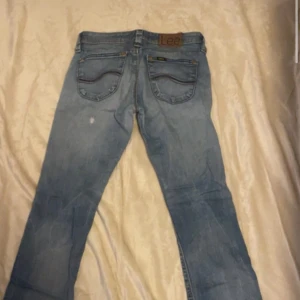 Lee Maddox ljusblå jeans W28 L31 - Säljer ett par Lee Maddox jeans i ljusblå tvätt med klassiska femficksdetaljer och snygga kontrastsömmar. Jeansen har normal passform och raka ben, med Lee-logga på bakfickan och läderpatch i midjan. Perfekta för en avslappnad stil.