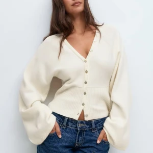 Vit kofta med v-ringning från Gina Tricot - Superfin vit kofta från Gina Tricot med v-ringning och snygga knappar framtill. Modellen är fulllång med bred ribbad midja och har långa, lite puffiga ärmar. Tillverkad i mjukt stickat material med polyester. Perfekt för lager-på-lager under hösten eller våren. Helt oanvänd! 