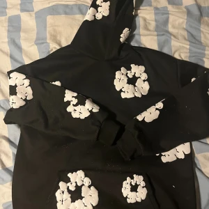 Svart hoodie med vita blommor - Svart hoodie med stora vita blommönster tryckta över hela tröjan, inklusive huvan och ärmarna. Tröjan har en klassisk huva och magficka framtill. Perfekt för dig som gillar streetwear med unik design.pris går att diskutera 