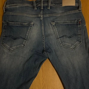 Blå Replay jeans - Liknar ambass i passform.                                           Snygga blå jeans från Replay med klassisk femficksdesign . Jeansen har ljusa slitningar framtill och bak, samt tydliga sömmar och Replay-logga på fickan. Perfekta för dig som gillar en avslappnad men trendig look.