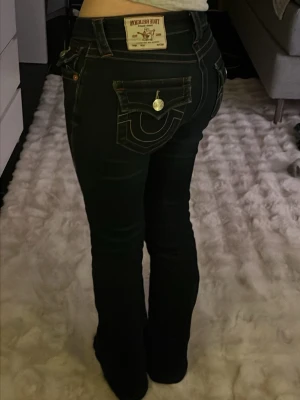 Mörkblåa true religion jeans - Säljer mina snygga true religion jeans. De har små rödgula detaljer och de är midrise men jag tycker de lutar mot lowrise. De är storlek 24 men är lite som mellan 24 och 25. Älskar dessa jeans och de är väldigt enkla att styla till vad som hällst. De har skygga detaljer bak och fram, alla knappar är kvar. De är inte så mycket använda och färgen har hållt sig som ny. Ska sälja de för att jag är pank och då de är smått för korta för mig.