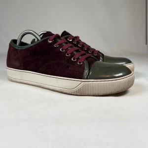Vinröda Lanvin sneakers i mocka - Säljer ett par stilrena Lanvin sneakers i vinröd mocka med mörkgrå tå i lack och matchande vinröda skosnören. Skorna har vit sula och metallfärgade öljetter. Perfekta för dig som vill ha något unikt och lyxigt till vardagslooken.