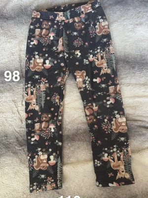 Svarta leggings med djurmönster, stl 98 - Mysiga svarta leggings med gulligt mönster av ekorrar, rådjur, svampar och blommor i bruna, beige och gröna toner. Perfekta för dig som gillar naturinspirerade prints och vill ha något bekvämt och lekfullt.🌸 Fint använt skick. Storlek 98