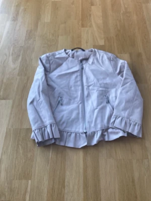 Ljusrosa skinnjacka med volang - Säljer en ljusrosa skinnjacka med dragkedja framtill och volangdetaljer vid ärmslut och nederkantfrån Zara. Jackan har två snedställda fickor med dragkedja och en clean, modern look. 