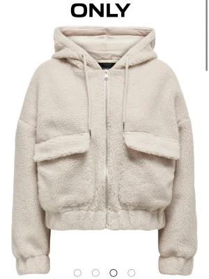 Vit teddyjacka med huva från ONLY - Mysig vit teddyjacka från ONLY med huva och stora fickor framtill. Jackan har dragkedja, snörning i huvan och en loose passform. Perfekt för dig som vill ha en varm och trendig look. Passar till både jeans och mjukisbyxor. Jag köpte den för 550 säljer den för 350 då den aldrig är använd. Pris kan diskuteras!