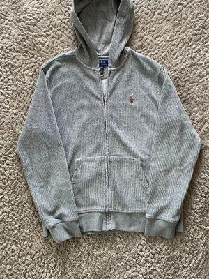 Polo ralph lauren hoodie - Säljer en riktigt snygg zip-hoodie från Polo Ralph Lauren i grå manchester. Materialet ger tröjan en unik textur och en lite mer "klädd" look än vanliga hoodies. Klassisk broderad logga på bröstet. Skriv ett DM om ni har fler frågor!