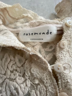 ✨ Elegant spetsblus från Rosemunde – S/XS ✨ - Vacker, romantisk spetsblus från Rosemunde Copenhagen i en ljus creme/ivory nyans. Figurnära modell med långa ärmar, dekorativa knappar framtill och vågig kant nedtill. Perfekt både till vardag och fest – lika fin till jeans som till kjol.
