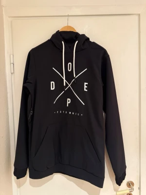 Svart skidjacka/snowboardjacka från Dope med tryck - Svart skidjacka/snowboardjacka Yeti från Dope med stort vitt tryck på bröstet och huva med snörning. Jackan har en stor magficka och elastiska muddar vid ärmslut och nederkant. Använd en gång så jackan är i nyskick. Finns på fler sidor. 