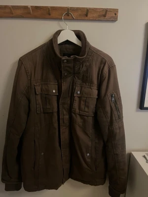 Fieldjacket Koroshi - Fieldjacket från koroshi med hög krage, flera fickor med knappar och dragkedja på ärmen. Passar bra till vår och höst 