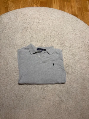 Grå långärmad pikétröja Polo Ralph Lauren - Säljer en stilren grå långärmad pikétröja från Polo Ralph Lauren i slim fit. Tröjan är köpt på själva Ralph Lauren hemsidan och kostade 1299. Storlek 14-16 år men passar de som har xs eller small.