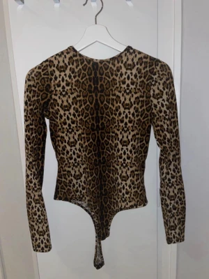 Leopardmönstrad topp från NA-KD - Säljer en leopardmönstrad långärmad topp från NA-KD i storlek 36. Toppen har djup v-ringning framtill och är figurnära med en cool asymmetrisk nederkant. Materialet är stretchigt och lätt, perfekt för att sticka ut.