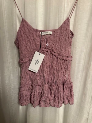 Ljuslila spetslinne från Stradivarius - Supersött ljuslila linne nästan rosa från Stradivarius med tunna axelband. Hela toppen är täckt av spets och har extra tjockt lager av tyg vid bysten. Den är i storlek S och är helt oanvänd med prislappen kvar.💞