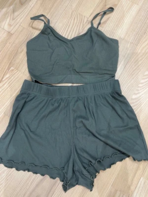 Grön ribbad pyjamasset - Säljer en grön croppad väst med smala axelband och ribbad struktur. Västen har en enkel, stilren design och är gjord i ett mjukt och stretchigt material som känns skönt mot huden. Perfekt att matcha med shorts eller jeans för en chill look.