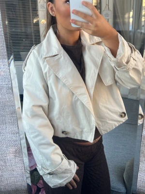 Beige trenchcoat  - Säljer min Snygga croppade trenchcoat i beige, stora dekorativa knappar och detaljer. Super fin att ha nu till hösten 