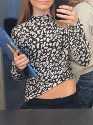 Svartvit leopardmönstrad polotopp - Säljer en svartvit polotopp med leopardmönster. Toppen har lång ärm och är croppad i modellen vilket ger en trendig look. Perfekt för dig som vill sticka ut med ett djurmönster i garderoben. Passar Xs/s
