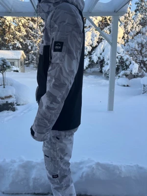 Dopesnow  jacka & byxor- komplett vintersett  - Jackan är en anorak med halv dragkedja, justerbar huva och midja samt flera praktiska fickor, inklusive bröstficka och ärm­ficka för liftkort. Ärmsluten är justerbara och passformen ger bra rörelsefrihet och värme.  Byxorna är fodrade, vind- och vattenavvisande samt slitstarka. De har två benfickor med lock, justerbar midja och är anpassade för skidpjäxor eller vinterkängor, med god rörlighet för skidåkning och snowboard. Det här vintersettet är perfekt för dig som vill sticka ut och vara varm. 