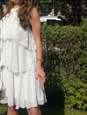 Vit omlottklänning med volanger - PRIS DISKUTERAS!! Supersöt vit kortklänning med flera lager volanger och omlottkänsla. Klänningen har halterneck med knutdetalj vid halsen och är ärmlös. Perfekt för sommarens alla tillfällen och ger en luftig och fräsch look.