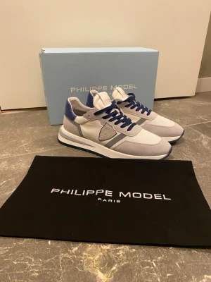 Philippe Model trainers - Snygga Philippe Model sneakers i vitt och blått med grå detaljer. Riktigt feta men köpte en storlek för lite så har bara provat dem och väljer nu att sälja dem här. Rekommenderar att man tar en storlek större när man köper dessa. Använt dem en gång så skicket är exemplariskt!