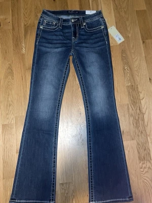 Blå bootcut jeans från Miss Me - Snygga blå bootcut jeans från Miss Me med kontrastsömmar och broderade bakfickor med pärldetaljer. Jeansen har midwaist och klassisk femficksdesign. Pris kan diskuteras!